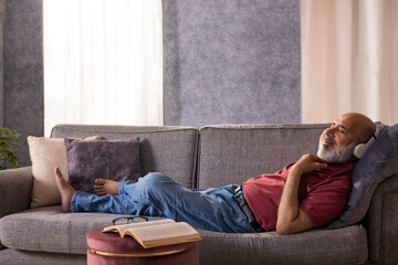 Senior man listening to music with headphone while lying on sofa at home