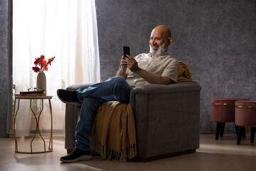 Senior man using mobile phone while sitting on sofa in living room