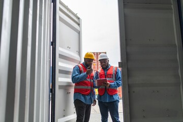 Fototapeta na wymiar Two black african male professional engineers doing routine checkup on a container logistic shipping yard ensuring all containers are following procedure and safety regulation