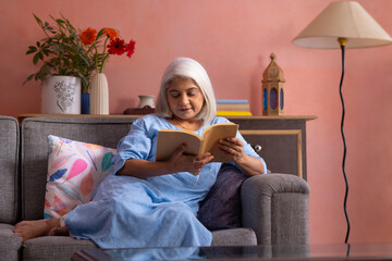 Portrait of an old woman reading a book in living room