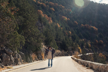 Woman walking along a road in an autumn beautiful forest on a sunny day. Vacation and travel concept.
