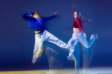  Portrait of young man and woman dancing hip-hop isolated over dark blue background with mixed lights. Jumping high © Lustre