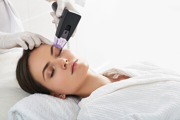 Brown haired woman receiving radiofrequency lifting procedure around eyes for her face skin rejuvenation at aesthetic cosmetology center - 544104997