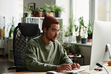 Young serious IT engineer working with coded information while sitting by desk in front of computer...