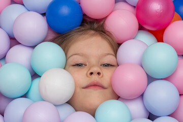 Fototapeta na wymiar Face of caucasian little girl of 6 years among multicolor balls in play center inside