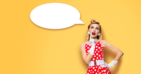 Studio portrait image of thinking woman in red pin up dress. Blond pinup thougthfull girl on yellow background. White empty blank speech sign bubble, having idea.