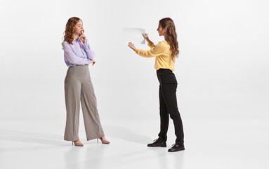 Naklejka premium Portrait of two women, employees working together, discussing business analytics isolated over white background