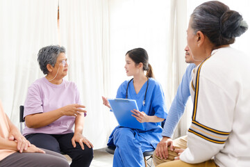 The caregiver therapist sits with a group of Asian senior people in a circle for checking physical...