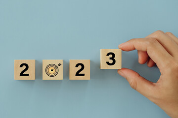 Hand putting wood cube numbers 3 on Wooden cubes with numbers 2023 and target icon on blue...