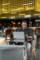 Portrait of handsome young African man using laptop computer in coffee shop - 544115331