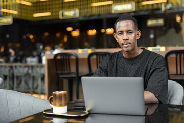 Fototapeta premium Portrait of handsome young African man using laptop computer in coffee shop