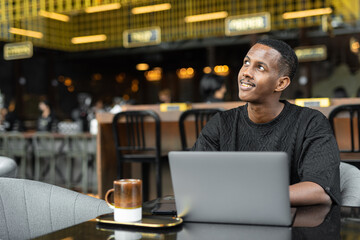 Obraz premium Portrait of handsome young African man using laptop computer in coffee shop