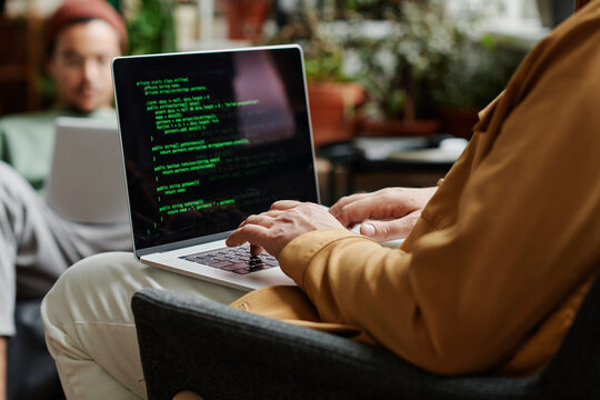 Mature professional IT engineer developing new software or decoding data on laptop scren while typing in front of young coworker