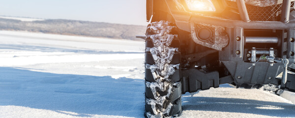 Front POV close-up detail view of quad bike offroad vehicle parked in snowdrift track on sunny...