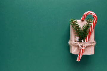 Top view flat lay on green background festive Christmas gift wrapped in craft paper decorated with candy red cane in white stripes and fir branches with snow, copy space, mockup. - Powered by Adobe
