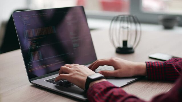 Close up of freelancer's hands typing code on laptop keyboard. Camera slides around developer's figers writing program code on computer display. Programmer working on online application database.