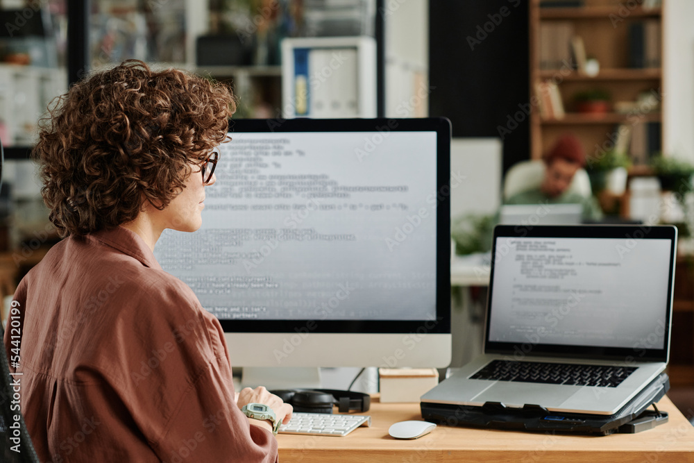Poster Young IT engineer looking at laptop screen with coded data and decoding it while developing new software in coworking space