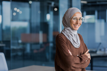 Portrait of successful and happy businesswoman in hijab, office worker smiling and looking at...
