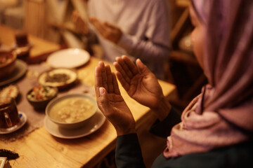 Close up of black Muslim woman praying during family meal at dining table.