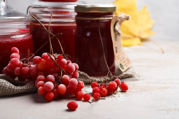 Viburnum fruit jam in glass jars with ripe red viburnum berries on white background, autumn preserves concept. close up.