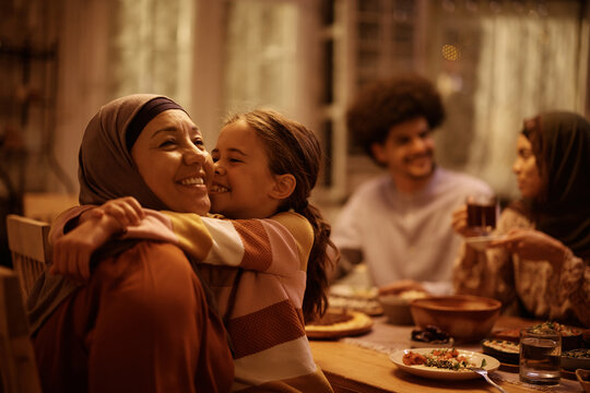 Happy Muslim little girl embracing her grandmother in dining room.