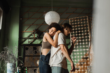 pretty african american woman with closed eyes embracing young artist in studio on blurred foreground.