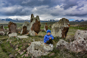 A little boy near a megalithic standing stone, Zorats karer or Karahunj is a prehistoric monument...