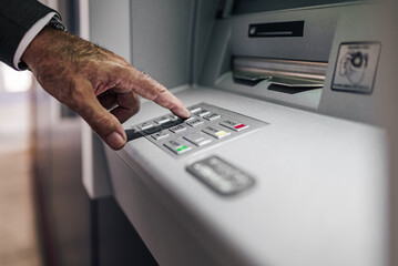 Cropped image of entrepreneur pushing buttons for entering PIN in ATM machine.