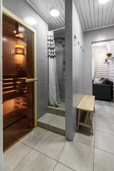 Finnish bathroom with a small wooden sauna and mosaic tile floor. Modern spa interior with glass door and Turkish towel