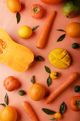Ripe and tasty orange and yellow fruits, carrots and pumpkin around coral color background. flat lay