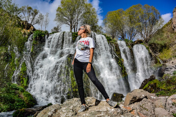 Obraz premium A young girl near the Shaki waterfall, with a height of 18 m. It is located in the Syunik region of Armenia, near the city of Goris. May 5, 2019