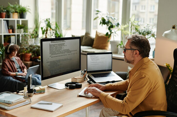 Serious businessman concentrating on decoding data while sitting by workplace in front of computer...
