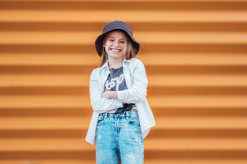 Little fashion-dressed girl portrait sincerely smiling while looking at camera on orange wall...