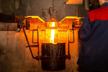 Pouring liquid metal from furnace into vat at metallurgical production. Metal part factory, foundry...