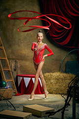 Retro circus performance. Little flexible girl, gymnast or acrobat doing gymnastics trick over dark...