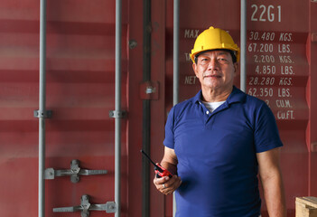 A male engineer holding a radio stands in front of a container. to inspect the containers before loading the goods for delivery