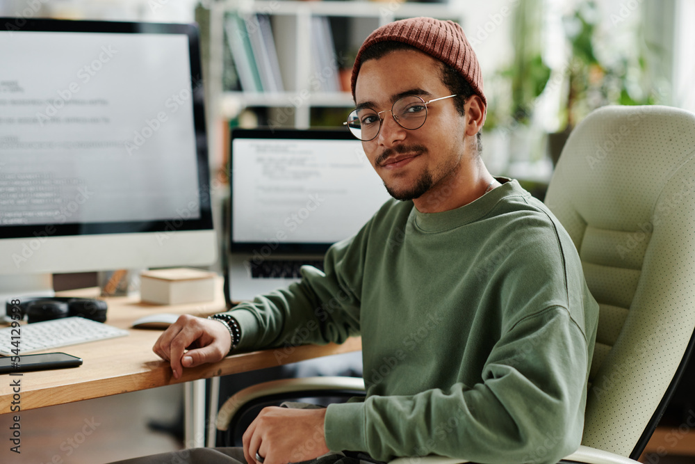 Poster young confident it engineer or software developer in casualwear sitting in armchair by computer moni