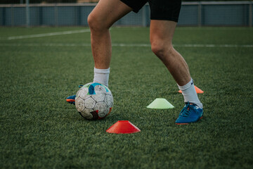 Vertical shot of player's legs dribbling cones on grass field.