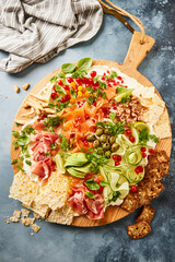 Large wooden board with cream cheese and several toppings like fresh salmon, cucumber, olives and shrimps.