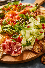 Closeup of a cheese board with slices of cucumber, avocado, fresh ham and tomatoes