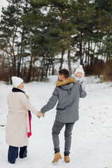 Family walking in the snow having fun in winter park on a bright day hugging each other and smiling