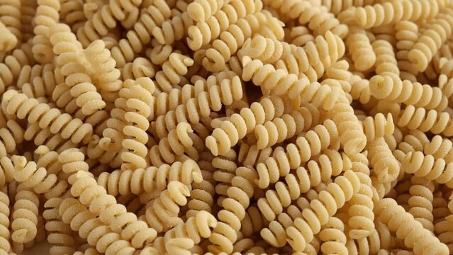 Gluten Free Cornmeal Pasta Wallpaper. Spiral Raw Macaroni from Blend of Corn and Rice flour rotating on Turntable. Close Up Top View. Uncooked Rotini Pasta is Spinning. Full Frame. Food Background. Ad