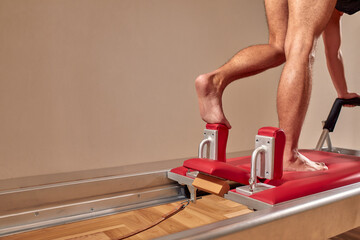 Side view of barefoot male athlete lying on pilates reformer and performing abs exercise during fitness workout. Pilates man concept.