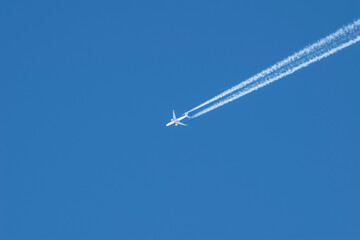 a white plane high in the blue sky leaves a trail