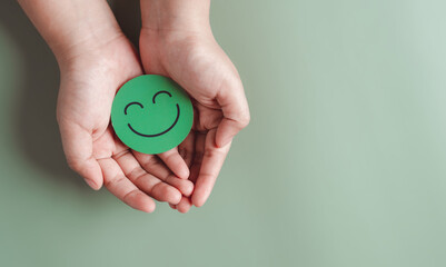 Hands holding green happy smile face, good feedback rating, positive customer review, experience, satisfaction survey, smiley mental health, child wellness, world mental health day on green background