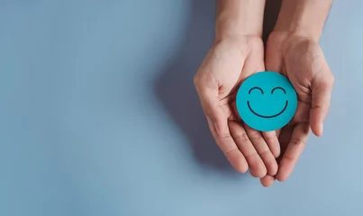 Fotobehang Hands holding blue happy smile face, good feedback rating, positive customer review, experience, satisfaction survey, smiley mental health, child wellness, world mental health day on blue background © Kiattisak