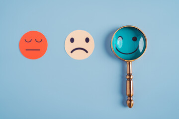 Hand holding magnifier focus selected happy smiley face paper cut which is among various emotions, good feedback rating and positive customer review, experience, satisfaction survey, mental health