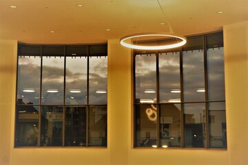 Innenraum von verglaster Gebäudehalle mit Raumdecke, leuchtender schwebender runder Lampe, gelbem...