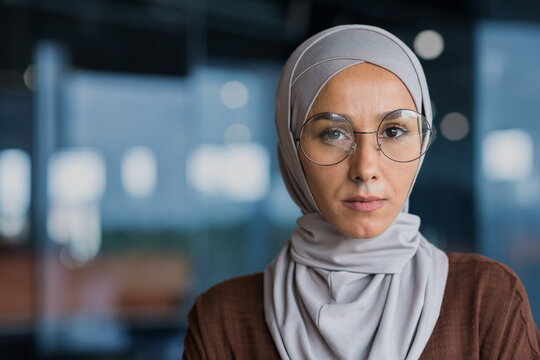 Closeup photo portrait of successful thinking business woman wearing hijab and glasses, woman looking at camera working inside modern office building.