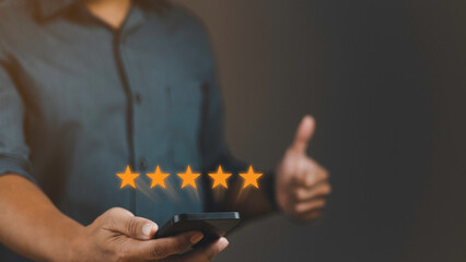 Customer review satisfaction feedback survey concept. User give rating to service experience on online application. Man using smartphone with five stars and showing thumbs-up.